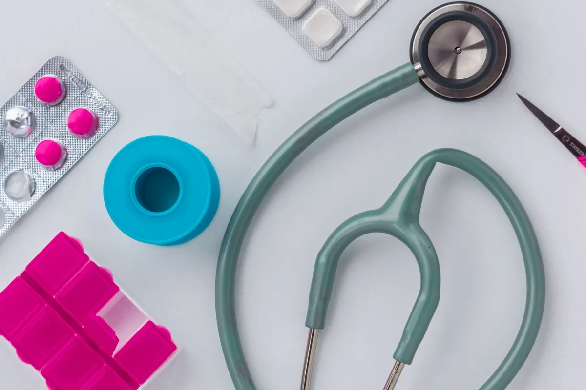 A stethoscope with pills and medication on a white table